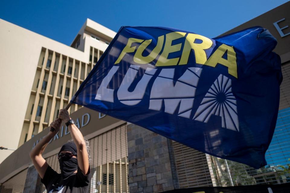 A woman waves a flag that reads in Spanish ‘LUMA Out’ during a protest in front of the headquarters of LUMA Energy (AFP via Getty Images)