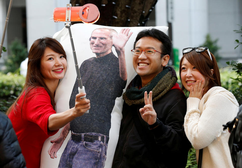 Ayano Tominaga (L) and other customers pose for a selfie photo with a cushion printed with a portrait of Apple co-founder Steve Jobs on it, as they wait in queue for the release of Apple’s new iPhone X in front of the Apple Store in Tokyo’s Omotesando shop