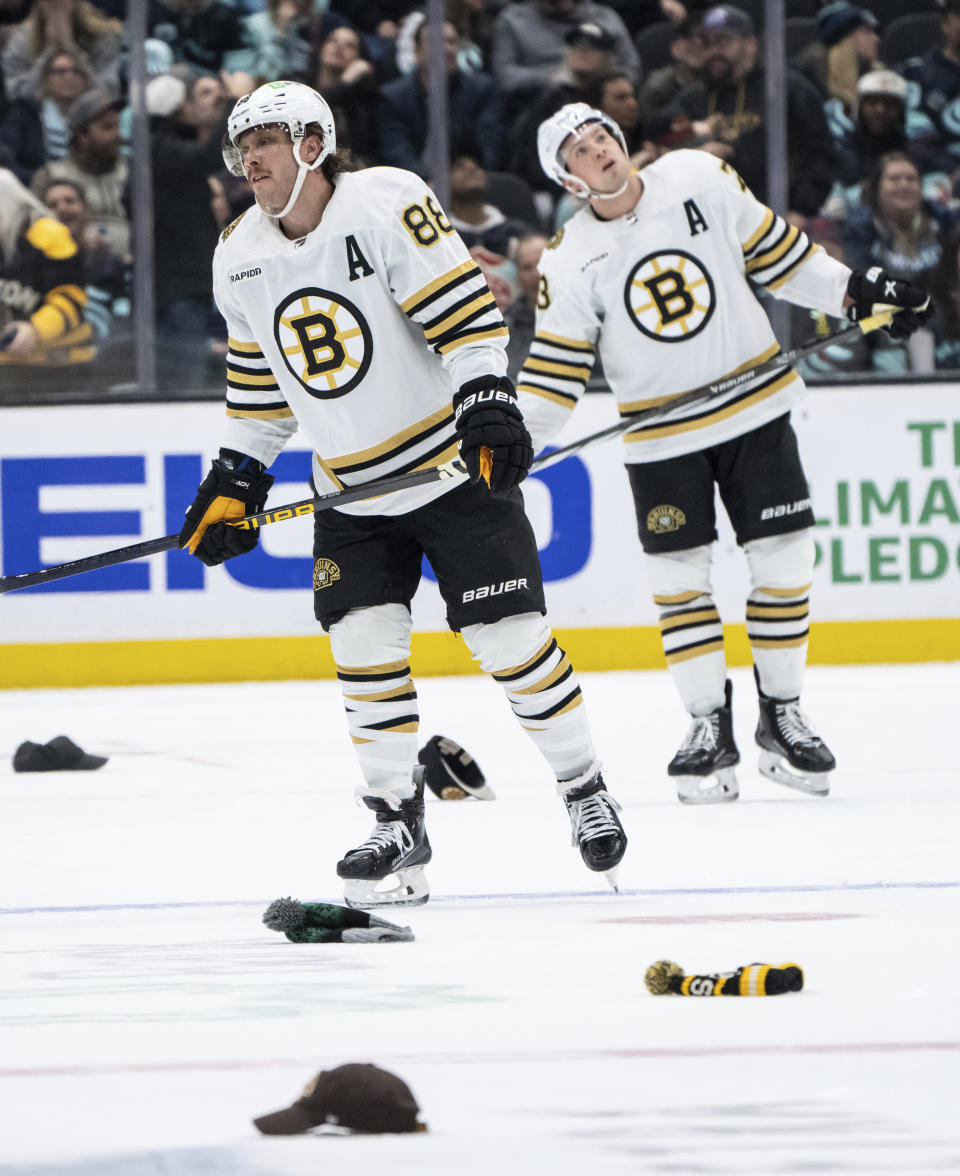 Boston Bruins forward David Pastrnak, left, skates among hats after scoring his third goal during the third period of an NHL hockey game against the Seattle Kraken, Monday, Feb. 26, 2024, in Seattle. The Kraken won 4-3 in a shootout. (AP Photo/Stephen Brashear)