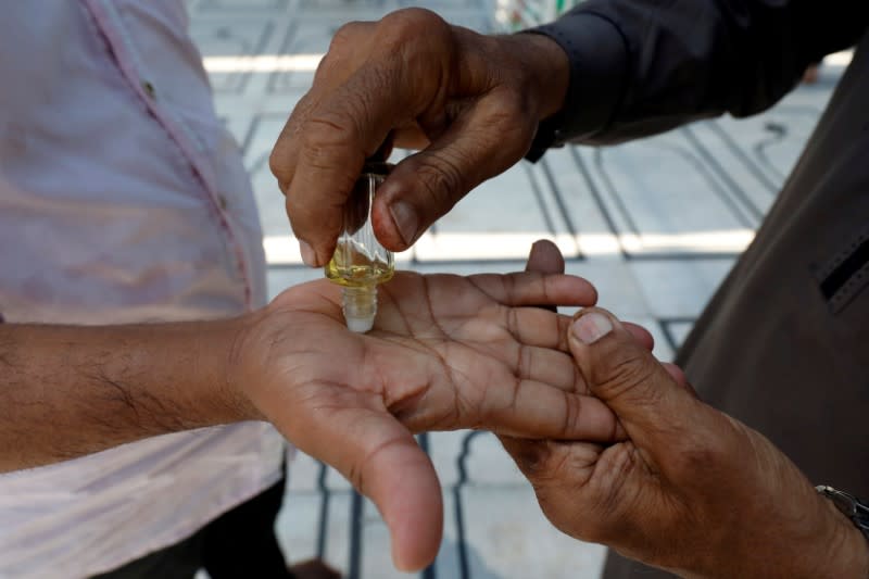 A man applies Ittar or oil perfume to another as they attend Friday prayer amid an outbreak of the coronavirus disease (COVID-19), at a mosque entrance in Karachi