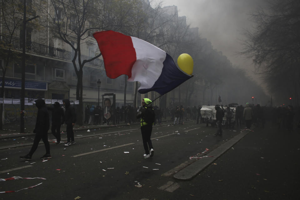 A man waves a French flag during a demonstration in Paris, Thursday, Dec. 5, 2019. Small groups of protesters are smashing store windows, setting fires and hurling flares in eastern Paris amid mass strikes over the government's retirement reform. (AP Photo/Rafael Yaghobzadeh)