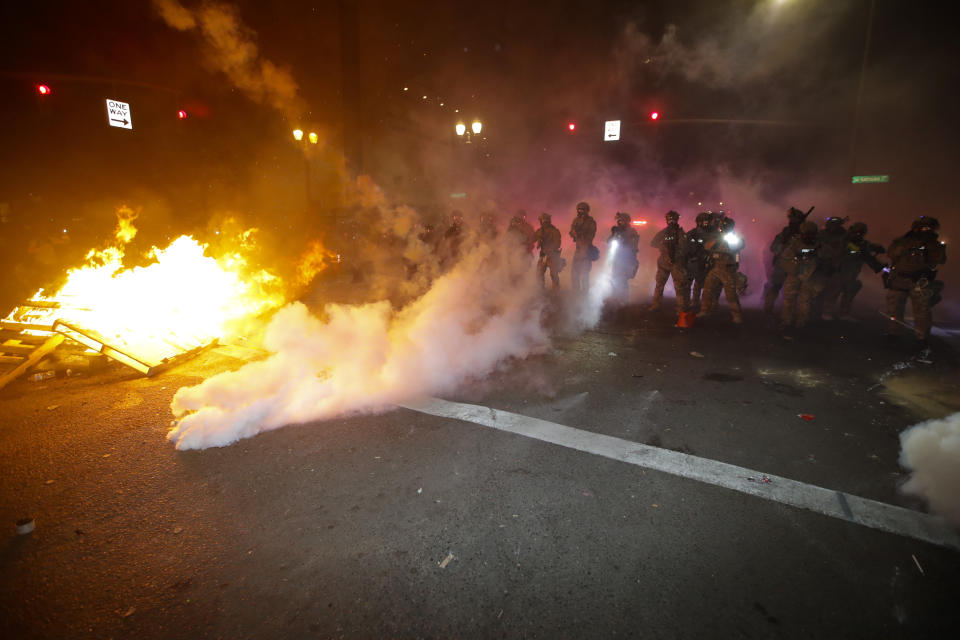 Federal officers clear a street where demonstrator had set a fire during a Black Lives Matter protest at the Mark O. Hatfield United States Courthouse Saturday, July 25, 2020, in Portland, Ore. (AP Photo/Marcio Jose Sanchez)