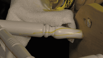 Close-up of a person's hand applying Goo Gone to a wooden chair to remove dried up glue