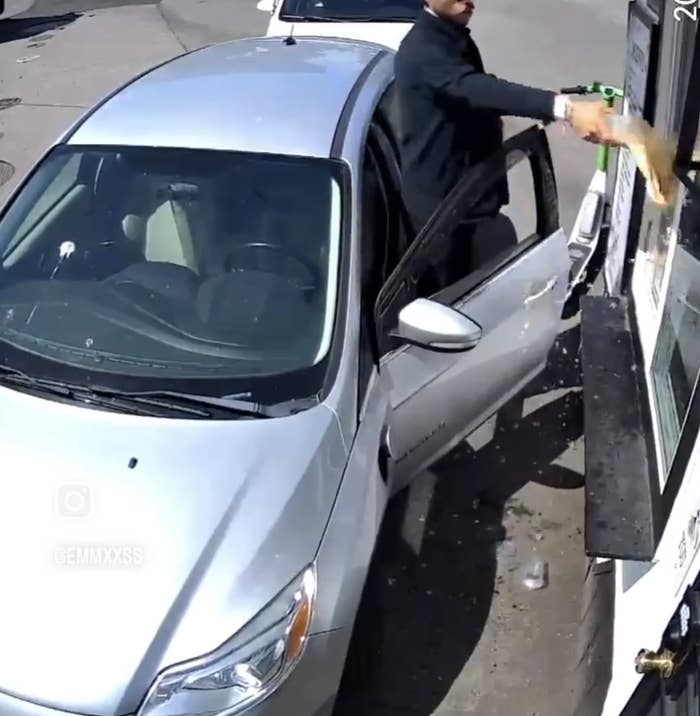 A man in a suit throws a takeaway bag back through a fast-food drive-thru window while standing next to a car. Image tagged with @GEMMXSS