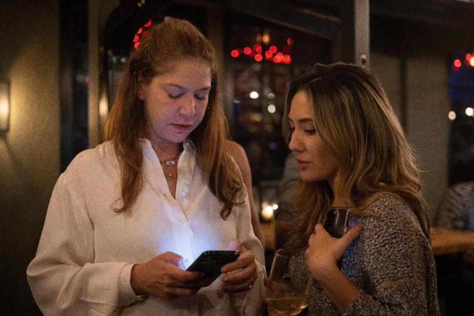 Incumbent Commissioner Sabina Covo, left, looks up results with a supporter during her watch party on Tuesday, Nov. 7, 2023, at Taurus in Coconut Grove. Covo and opponent Damian Pardo will be in a runoff election.