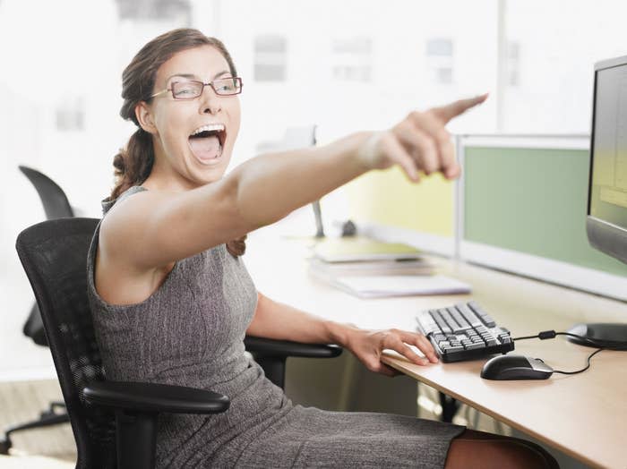 A woman pointing and laughing at her desk