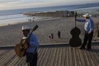 Musicians called "Talismanes de Tijuana" wait for customers near the border structure between Mexico and the U.S. at the Pacific Ocean, Tijuana, Mexico, Friday, Nov. 16, 2018. As thousands of migrants in a caravan of Central American asylum-seekers converge on the doorstep of the United States, what they won't find are armed American soldiers standing guard. (AP Photo/Rodrigo Abd)