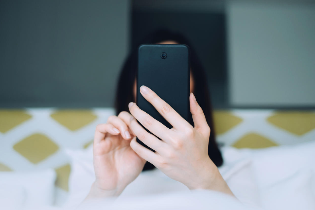 A pair of hands hold attached to a person in bed holds a smartphone facing the subject's hidden eyes.