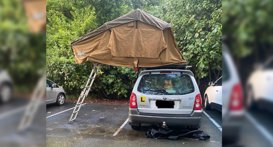 Tourists at Woods Bay in Noosa Heads park over two parking spaces with a tent and ladder extending over the spaces. 