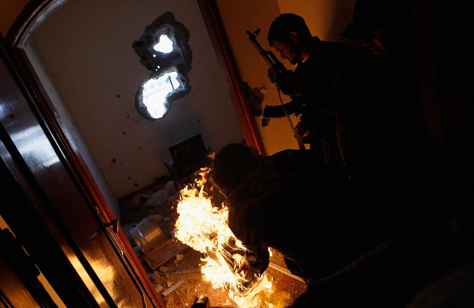 <p>Libyan rebel fighter rolls a burning tire into a room containing ensconced government loyalist troops who were firing on them during house-to-house fighting on Tripoli Street in downtown Misrata April 20, 2011 in Misrata, Libya. Rebel forces assaulted the downtown positions of troops loyal to Libyan strongman Moammar Gaddafi April 20, briefly forcing them back over a key bridge and trapping several in a building that fought back instead of surrendering, firing on the rebels in the building and seriously wounding two of them during the standoff. Fighting continued between Libyan government forces that had surrounded the city and anti-government rebels ensconced there. (Photo by Chris Hondros/Getty Images) </p>