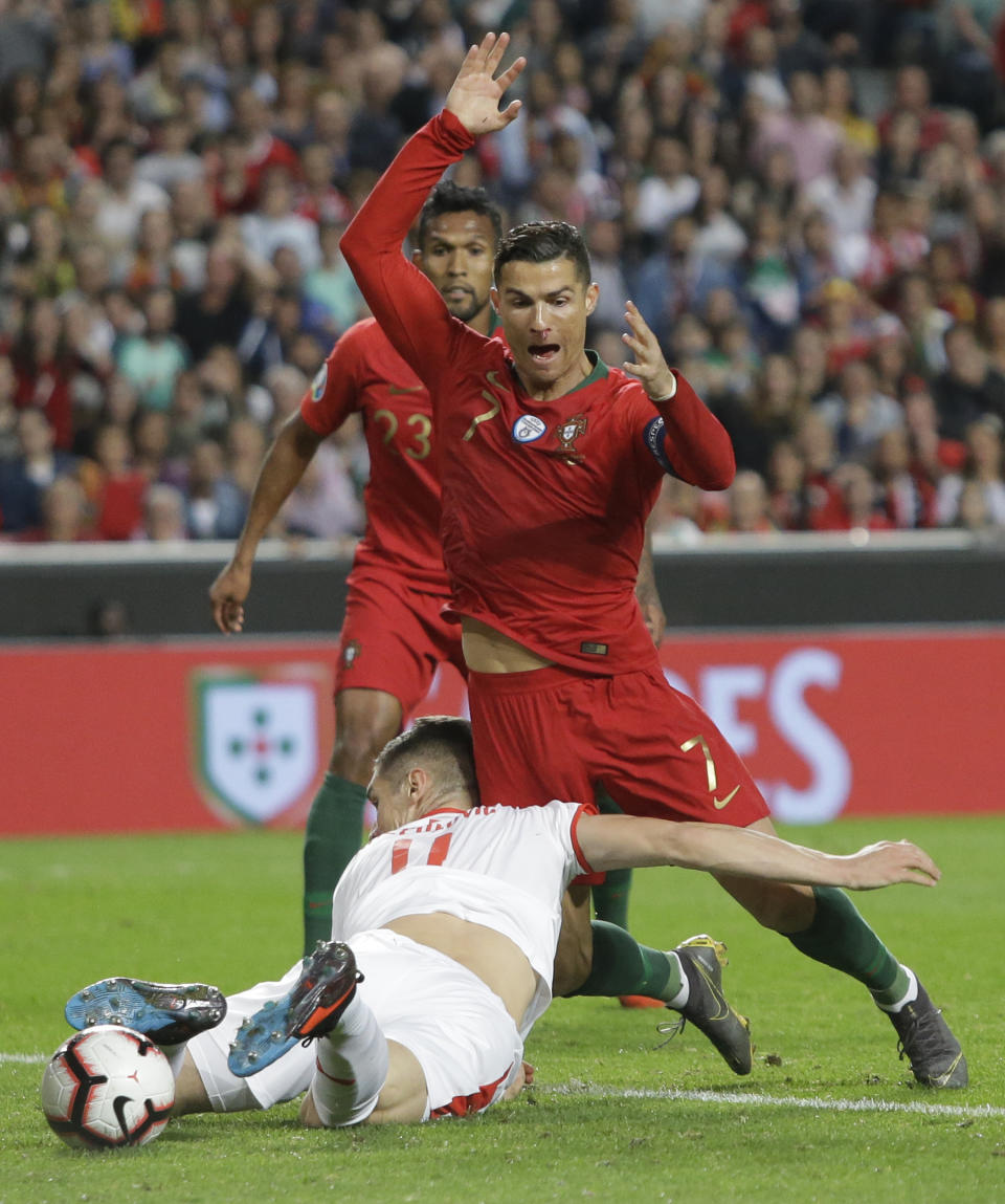 Serbia's Nikola Milenkovic, bottom, and Portugal's Cristiano Ronaldo challenge for the ball during the Euro 2020 group B qualifying soccer match between Portugal and Serbia at the Luz stadium in Lisbon, Portugal, Monday, March 25, 2019. (AP Photo/Armando Franca)