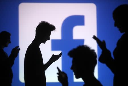 People are silhouetted as they pose with mobile devices in front of a screen projected with a Facebook logo, in this picture illustration taken in Zenica October 29, 2014. REUTERS/Dado Ruvic/Files