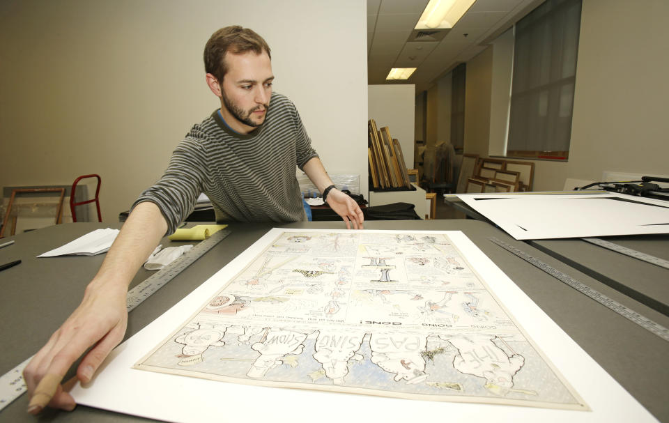 In this Wednesday, Oct. 23, 2013 photo, Jeremy Stone frames a Billy Ireland comic strip from Dec. 11, 1921 called "The Passing Show" at the Billy Ireland Cartoon Library & Museum in Columbus, Ohio. Today the museum collection includes more than 300,000 original strips from everybody who’s anybody in the newspaper comics world, plus 45,000 books, 29,000 comic books and 2,400 boxes of manuscript material, correspondence and other personal papers from artists. (AP Photo/Tony Dejak)