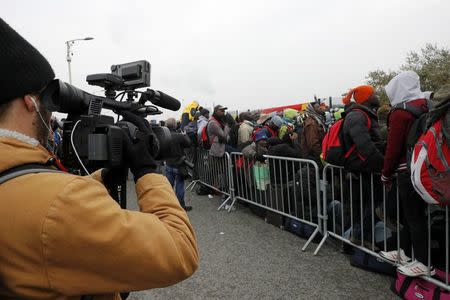 A TV cameraman films as migrants with their belongings queue at the start of their evacuation and transfer to reception centers in France, and the dismantlement of the camp called the "Jungle" in Calais, France, October 24, 2016. REUTERS/Philippe Wojazer
