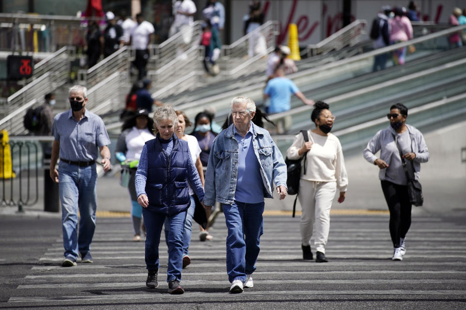 Masked and unmasked pedestrians walk across Las Vegas Boulevard, Tuesday, April 27, 2021, in Las Vegas. The Centers for Disease Control and Prevention eased its guidelines Tuesday on the wearing of masks outdoors, saying fully vaccinated Americans don't need to cover their faces anymore unless they are in a big crowd of strangers. (AP Photo/John Locher)