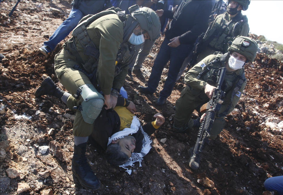 Israeli soldiers arrest a Palestinian during a protest against the expansion of Jewish settlements near the West Bank town of Salfit, Monday, Nov. 30, 2020. In years to come, Israelis will be able to commute into Jerusalem and Tel Aviv from settlements deep inside the West Bank via highways, tunnels and overpasses that cut a wide berth around Palestinian towns. Rights groups say the new roads that are being built will set the stage for explosive settlement growth, even if President-elect Joe Biden's administration somehow convinces Israel to curb its housing construction