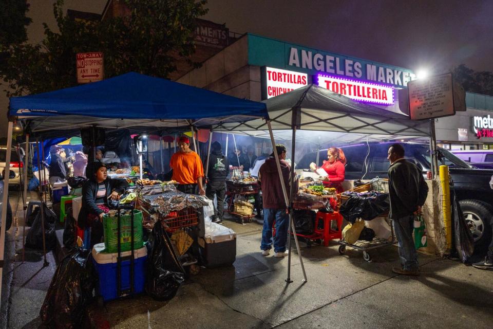 Customers wait to order and receive food cooked on a makeshift grill set up on the sidewalk