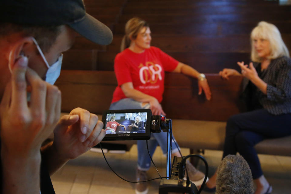 Teresa Stanfield, seated at center, the Oklahoma field director with Virginia-based Prison Fellowship, and Teresa Peden, right, pastor of recovery ministry at Crossing Community Church, are pictured in the camera display of videographer Drew Darby, left, Tuesday, Aug. 11, 2020, in Oklahoma City. Normally, Stanfield is behind bars, talking with inmates about how she changed the course of her troubled life. The coronavirus has forced her out of prisons. For the time being, Stanfield is videotaping her message. (AP Photo/Sue Ogrocki)