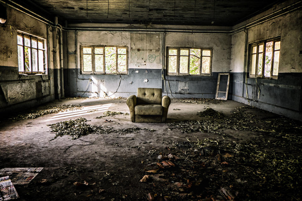 Abandoned house with leaves all over the floor and a deserted arm chair