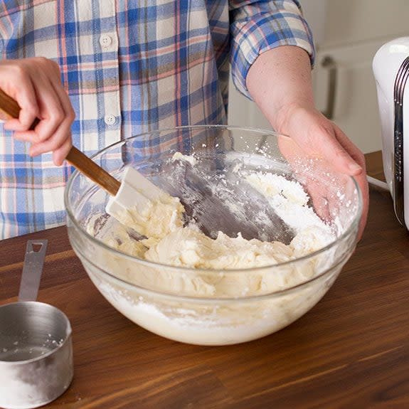 Person using a spatula to wipe the excess frosting from the sides of their glass bowl