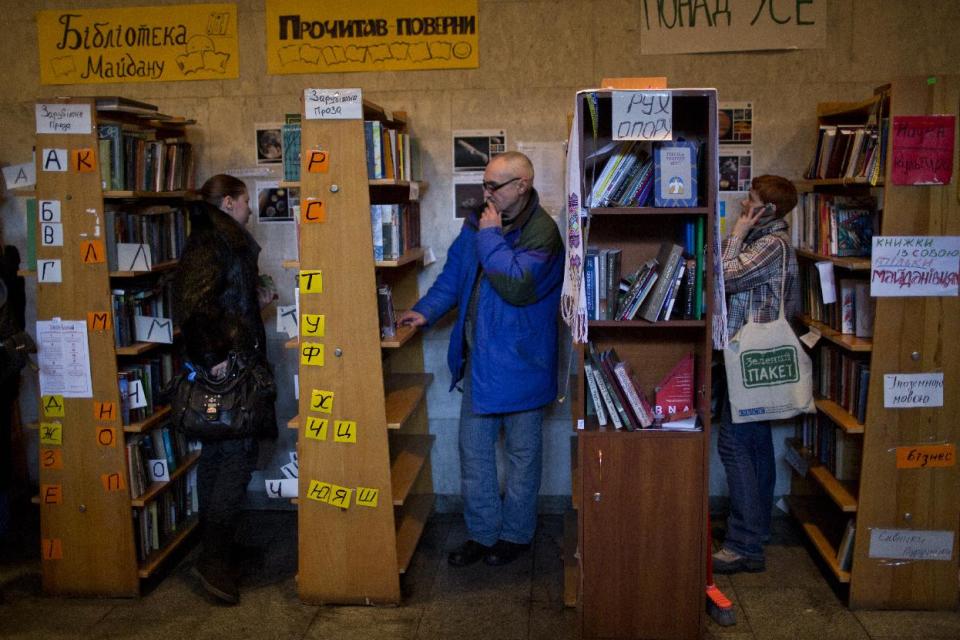 In this photo taken on Thursday, Feb. 6, 2014, Ukrainian protesters look at books organized on shelves in an improvised library set inside the Ukrainian House in Kiev. When the fervor flags for the protesters in Ukraine’s capital and they want to get away from the barricades for a little while, many of them are heading to an improvised library in one of the buildings seized by demonstrators. (AP Photo/Emilio Morenatti)