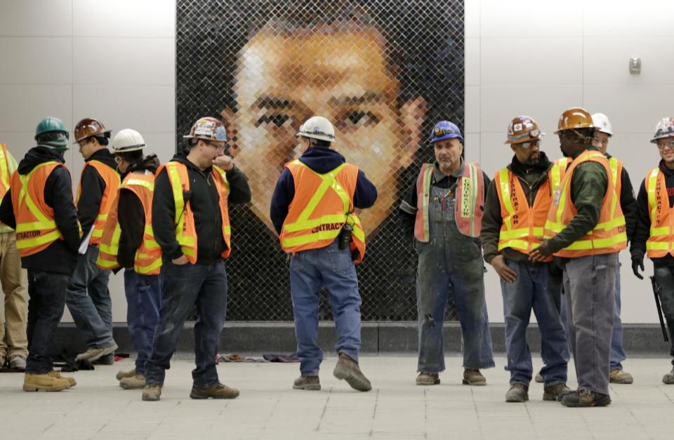 FILE- In this Dec. 22, 2016 file photo, construction workers stand in front of a mosaic by artist Chuck Close at the new 86th Street subway station on the Second Avenue line in New York. The first phase of the new Second Avenue subway, which has three stops, opens on Sunday, Jan. 1, 2017. (AP Photo/Seth Wenig, File)