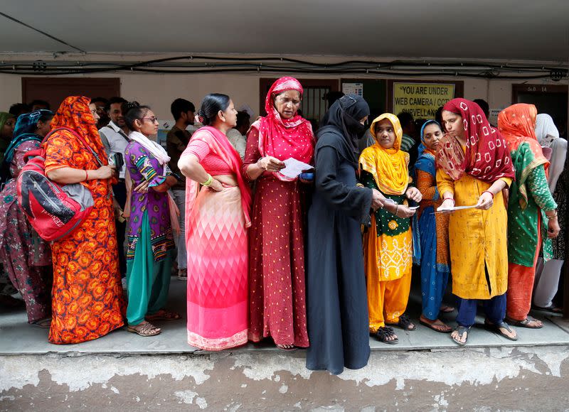 People wait in queues to cast their votes at a polling station, in Ahmedabad