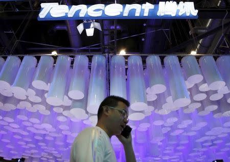 A man uses a mobile phone in front of a logo of Tencent at the Global Mobile Internet Conference (GMIC) 2015 in Beijing, China, April 28, 2015. REUTERS/Kim Kyung-Hoon