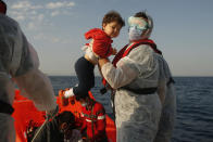 A Turkish coast guard officer, wearing protective gear to help prevent the spread of coronavirus, carries a child off a life raft during a rescue operation in the Aegean Sea, between Turkey and Greece, Saturday, Sept. 12, 2020. Turkey is accusing Greece of large-scale pushbacks at sea — summary deportations without access to asylum procedures, in violation of international law. The Turkish coast guard says it rescued over 300 migrants "pushed back by Greek elements to Turkish waters" this month alone. Greece denies the allegations and accuses Ankara of weaponizing migrants. (AP Photo/Emrah Gurel)