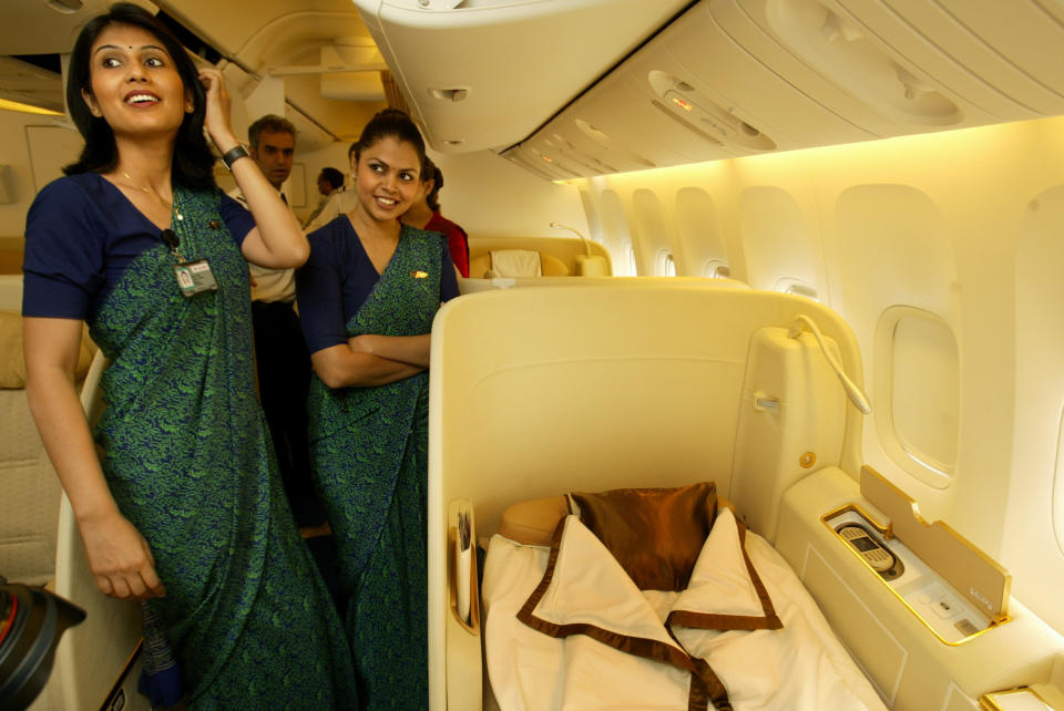 FILE - In this July 30, 2007, file photo, Air India's stewardesses explain facilities available to First Class travelers in their Boeing 777-200 LR aircraft during a function held to mark its commencement of operations, at the Chattrapati Shivaji International airport in Mumbai, India. Cash-starved Air India is putting its crew on a diet, changing their inflight menu to special low-fat meals. Dhananjay Kumar, the state-run airline's spokesman, said Wednesday, Sept. 18, 2019, that the objective is to provide healthy and cost-effective meals to crews on domestic and international flights. In 2009, the airline fired 10 air hostesses for being overweight after they failed to get back in shape three years after they were switched to ground crew jobs. (AP Photo/Gautam Singh, File)