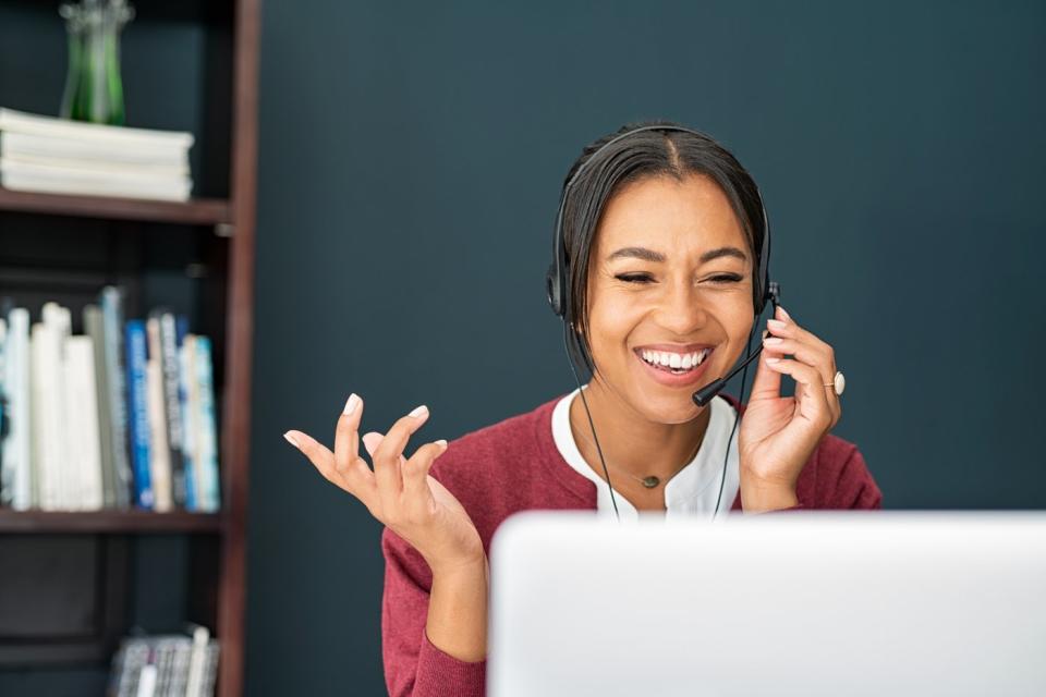 A smiling person wearing a telephone headset while looking at a laptop.