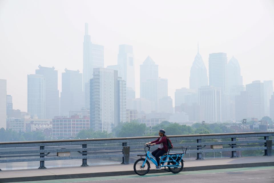 A person cycles past the skyline in Philadelphia shrouded in haze, Thursday, June 8, 2023. Intense Canadian wildfires are blanketing the northeastern U.S. in a dystopian haze, turning the air acrid, the sky yellowish gray and prompting warnings for vulnerable populations to stay inside.
