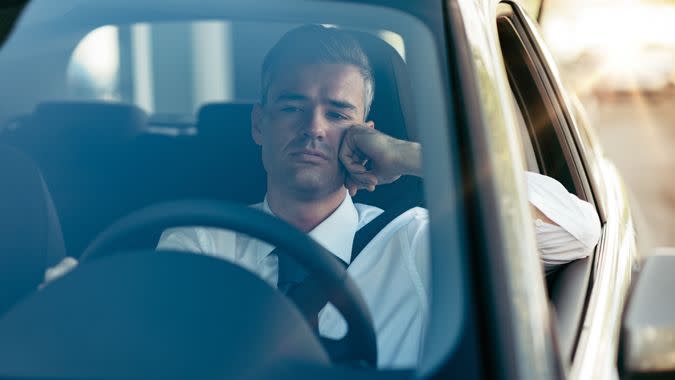 Pensive disappointed businessman sitting in his car and thinking with hand on chin.
