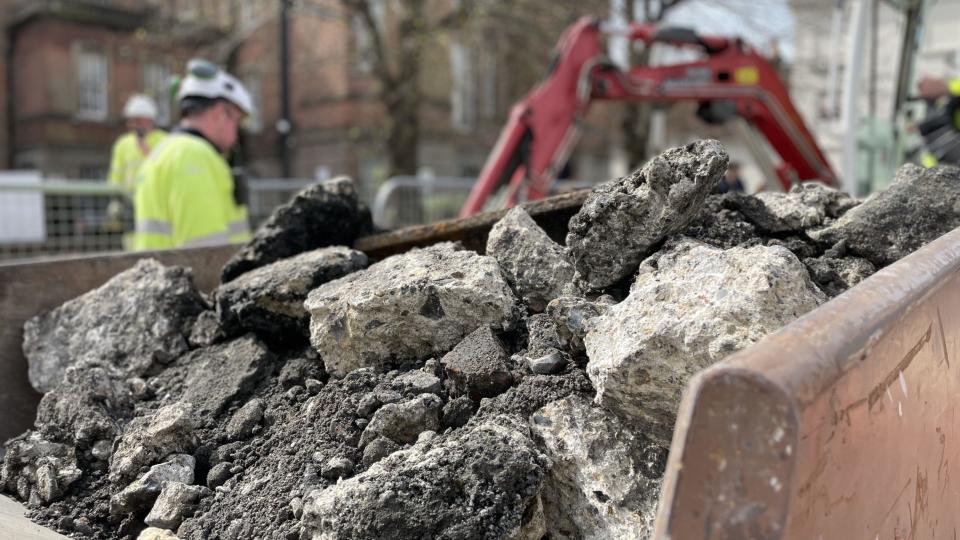 A skip full of rubble with workers and a digger blurred in the background on Fisherton Street, Salisbury