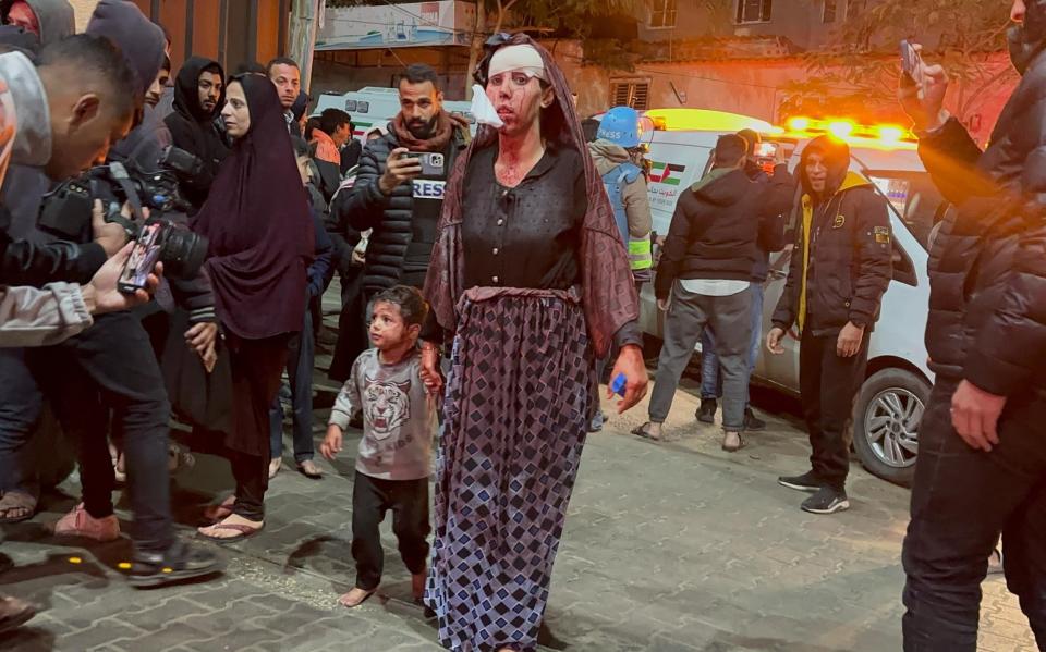 An injured woman covered in blood holds a child's hand, also injured, at Kuwait Hospital