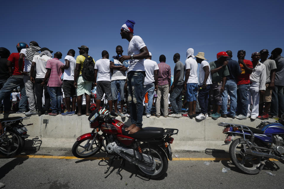 Protesters climb up on motorcycles and a highway barrier to try to get a look at thousands of demonstrators coming to join the march, in Petion-Ville, Port-au-Prince, Haiti, Sunday, Oct. 13, 2019. Thousands of Haitians joined a largely peaceful protest called by the art community Sunday to demand Moïse resign, increasing pressure on the embattled leader after nearly a month of marches that have shuttered schools and businesses.(AP Photo/Rebecca Blackwell)