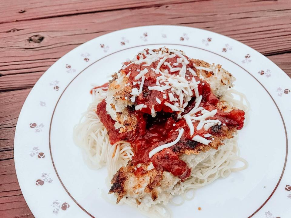 chicken parmesan over angel hair pasta on a white plate