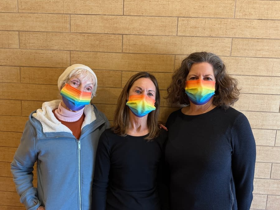 Three women stand side by side while wearing rainbow-colored face masks