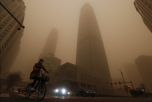 A cyclist and motorists move past office buildings amid a sandstorm during the morning rush hour in the central business district in Beijing, Monday, March 15, 2021. The sandstorm brought a tinted haze to Beijing's skies and sent air quality indices soaring on Monday. (AP Photo/Andy Wong)