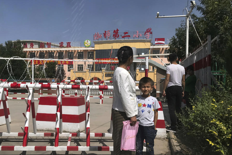 FILE - In this Aug. 31, 2018, file photo, a child and a woman wait outside a school entrance mounted with surveillance cameras and barricades with multiple layers of barbed wire in Peyzawat, western China's Xinjiang region. The Chinese database Victor Gevers found online was not just a collection of old personal details. The discovery by Gevers, a Dutch cybersecurity researcher who revealed it on Twitter last week, has given a rare glimpse into China’s extensive surveillance of Xinjiang, a remote region home to an ethnic minority population that is largely Muslim. The area has been blanketed with police checkpoints and security cameras that apparently are doing more than just recording what happens. The database Gevers found appears to have been recording people’s movements tracked by facial recognition technology, he said, logging more than 6.7 million coordinates in a span of 24 hours. (AP Photo/Ng Han Guan, File)