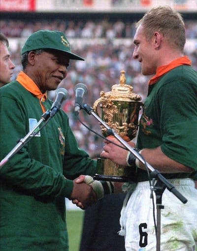 El capitán sudafricano de rugby Francois Pienaar recibe el trofeo de la Copa del Mundo de Rugby de manos del presidente Nelson Mandela después de que Sudáfrica derrotara a Nueva Zelanda en junio de 1995. (AP Photo / Ross Setford)