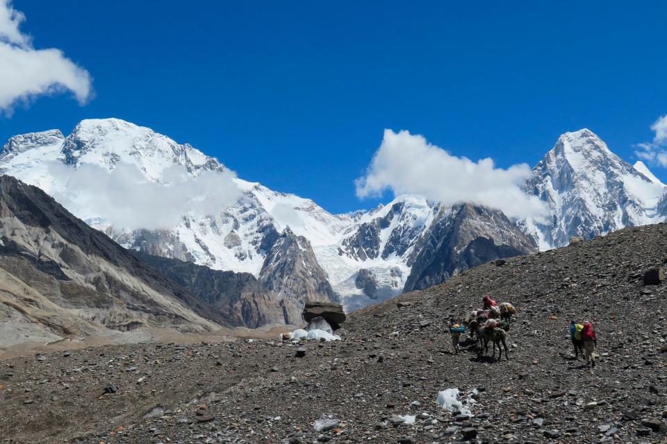 In this picture taken on August 14, 2019, porters and foreign trekkers move with mules towards the Concordia camping site. Broad Peak and Gasherbrum IV loom in the distance.