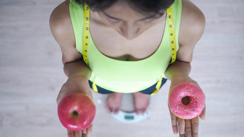 woman on weight scale with apple and donut