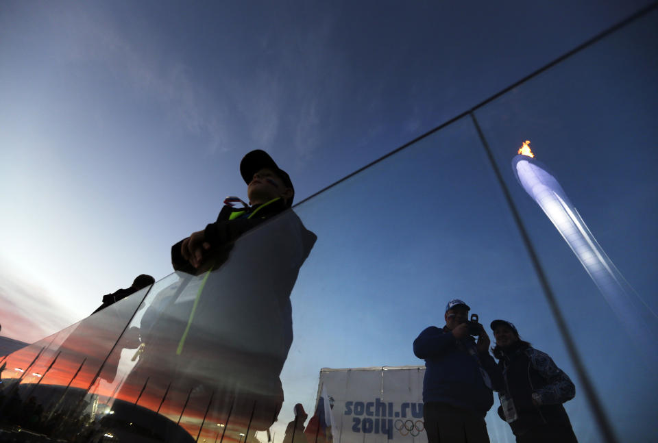 The Olympic cauldron is reflected in a glass partition at right as spectators gather on the Olympic Plaza at the 2014 Winter Olympics, Thursday, Feb. 13, 2014, in Sochi, Russia. (AP Photo/David Goldman)