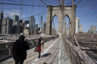 In this March 16, 2020 photo, Ines Tshiyomba, center, poses as her friend Garethe Mawonso takes her photo on the Brooklyn Bridge which is normally packed with tourists and commuters in New York. As of Sunday, nearly 2,000 people with the virus have been hospitalized in the state of New York and 114 have died, officials said. More than 15,000 have tested positive statewide, including 9,000 in New York City. (AP Photo/Mark Lennihan)