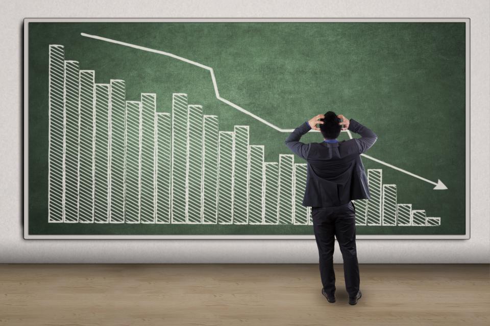 Man watching stock chart on chalkboard decline, has hands in hair, clearly stressed.