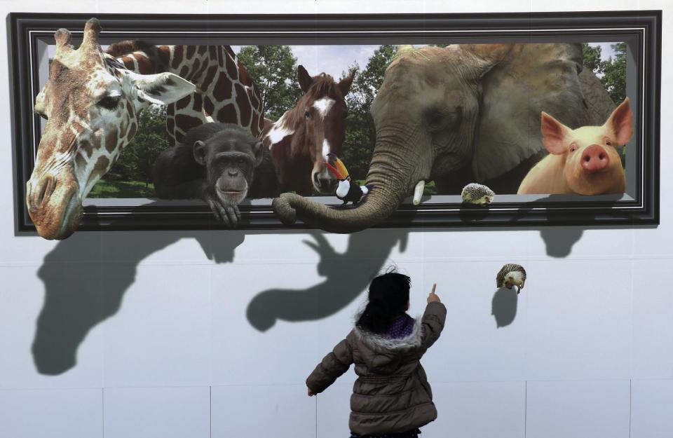 In this Sunday, Feb. 19, 2017 photo, a girl reacts to a 3D drawing of animals on the safety wall at a construction site of the archery venue for the Tokyo 2020 Summer Olympics in Tokyo. (AP Photo/Shizuo Kambayashi, File)