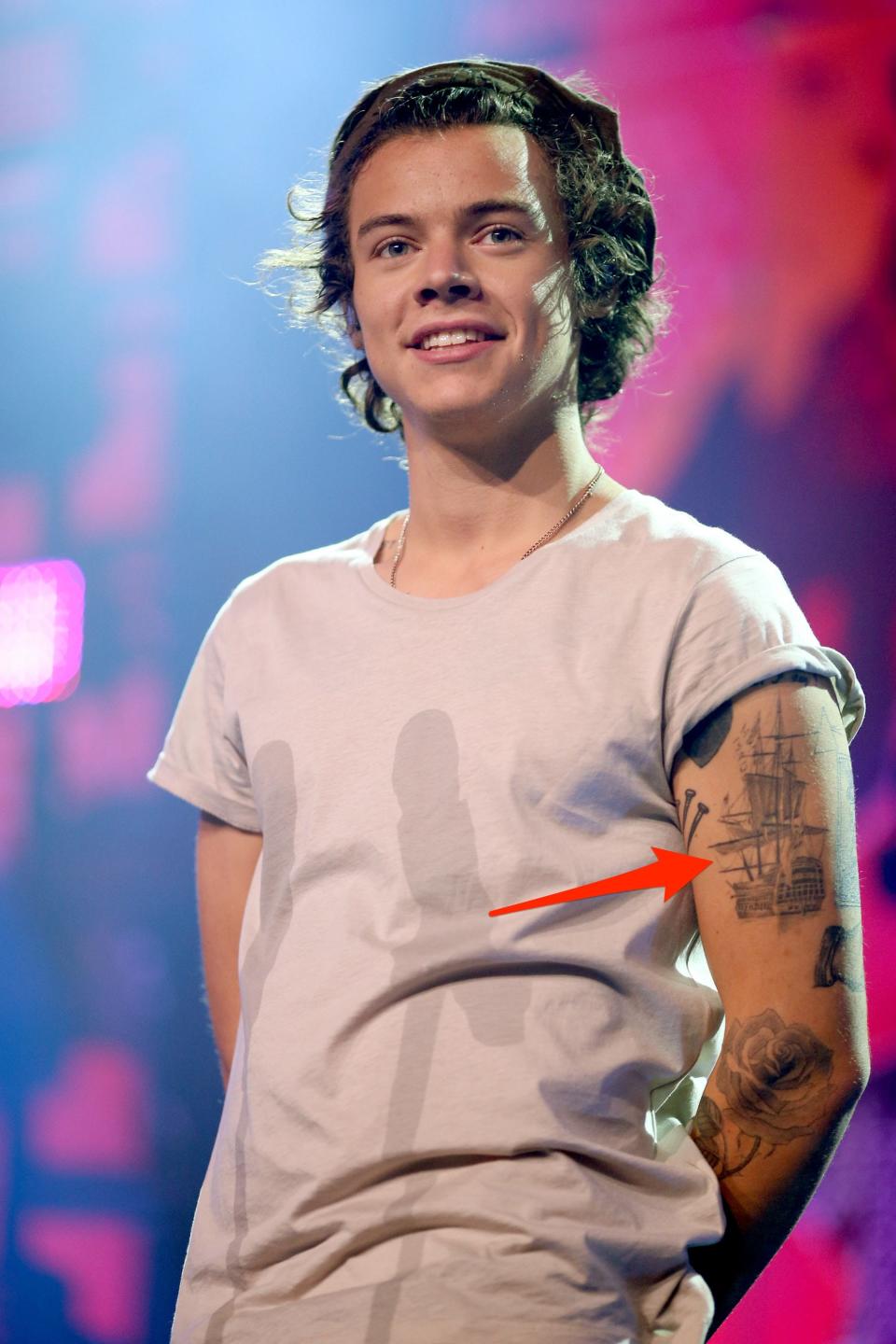 A red arrow pointing to Harry Styles' ship tattoo on his left bicep.