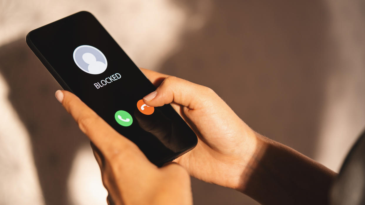  Smartphone held in person's hands displaying Blocked on incoming call screen 