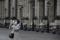 A tourist wearing a mask makes a selfie outside the Louvre museum Friday, Feb. 28, 2020 in Paris. . The world is scrambling to get on top of the new coronavirus outbreak that has spread from its epicenter in China to most corners of the planet. Governments and doctors are presenting an array of approaches as the virus disrupts daily routines, business plans and international travel around the world. (AP Photo/Rafael Yaghobzadeh)